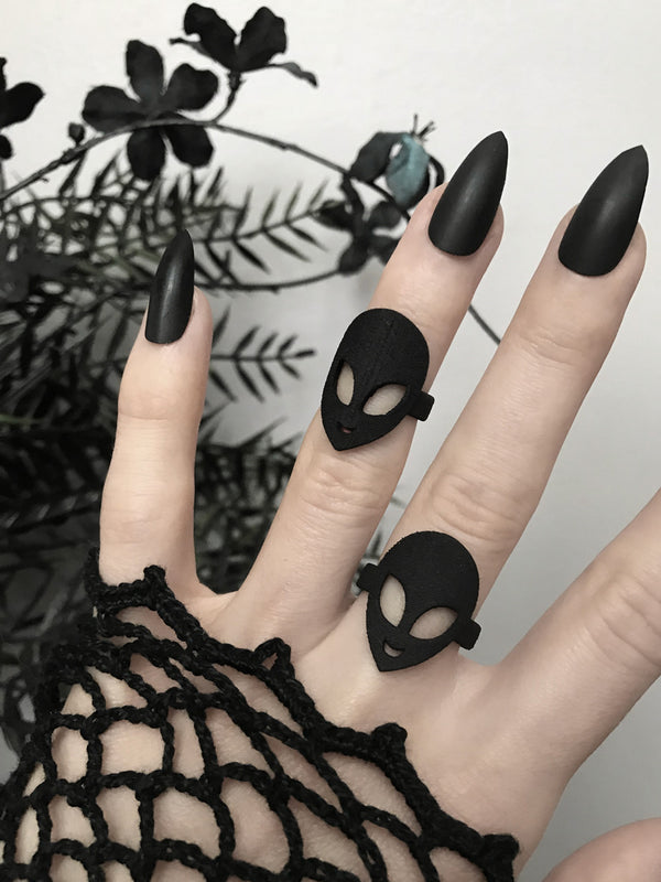Black ring with classic 90s alien face displayed on gothic model's hand with long black nails and witchy black flowers. 3d printed jewelry by Hypnovamp.