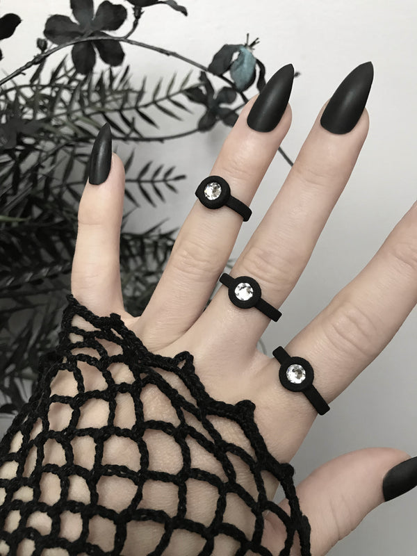 Simple matte black rings with white swarovski crystal stones, displayed on a gothic model's hand with long black nails. 3d printed jewelry by Hypnovamp.