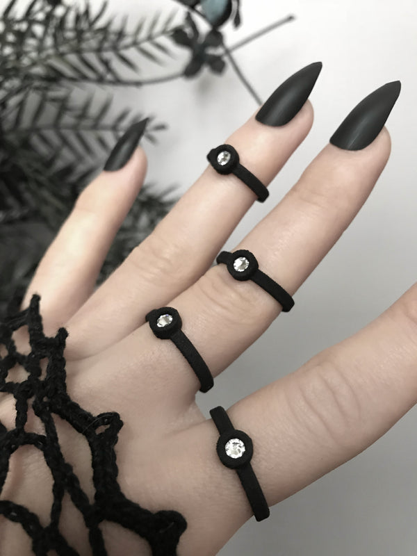 Close up of 4 simple matte black rings with white swarovski crystal stones, displayed on a gothic model's hand with long black nails. 3d printed jewelry by Hypnovamp.