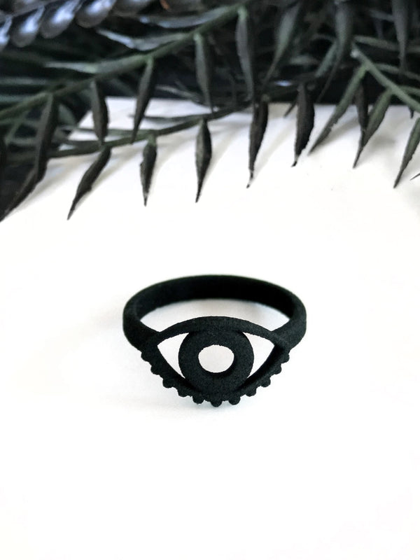 Bold graphic 3d printed black ring with evil eye design, displayed on white background with gothic black foliage border.
