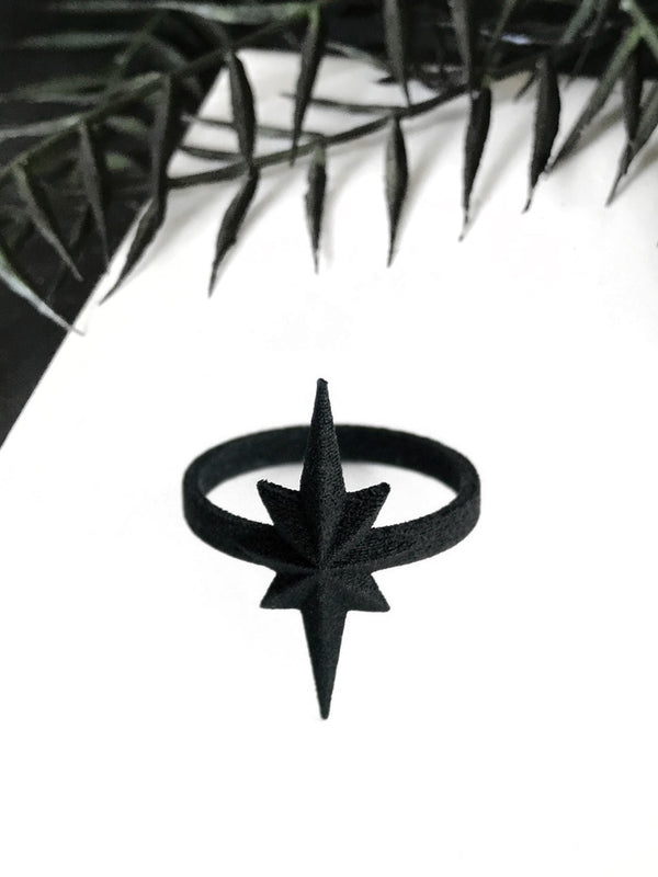 3d printed black atomic starburst ring on a white background with gothic foliage around the border. Mid-century style atomic jewelry by Hypnovamp.