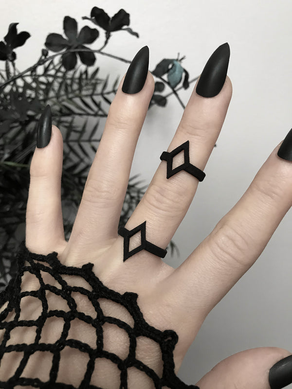 Bold graphic 3d printed black ring with diamond shaped outline design, displayed on gothic model hand with long black nails.