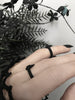 Matte black 3d printed goth ring with geometric pointy spike design, worn on a gothic model's hand with long pointy black nails. Side view.