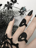 Side view of two black rings with classic 90s alien faces displayed on gothic model's hand with long black nails and witchy black flowers. 3d printed jewelry by Hypnovamp.