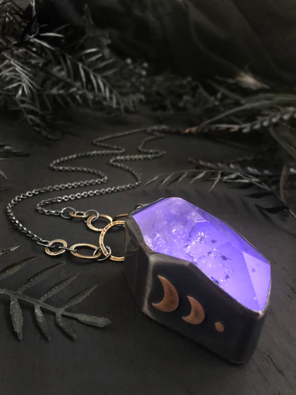 Purple glow in the dark crystal necklace with bronze moon details, displayed on a black foliage background. Handmade silver jewelry by Hypnovamp.