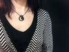 Matte black necklace with crescent moon and star design and swarovski crystal, displayed on a model wearing a black v neck shirt and a sweater with a black and white op art chevron pattern. Witchy 3d printed jewelry by Hypnovamp.