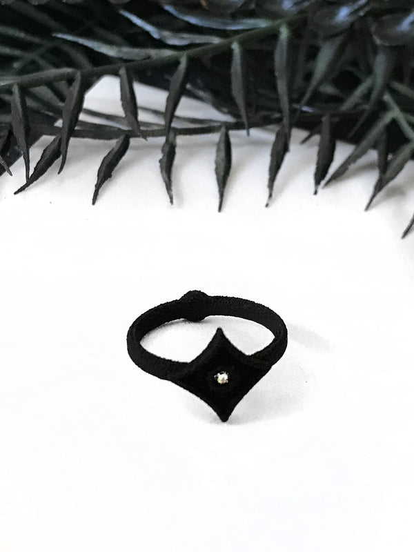 Matte black ring with atomic mid-century modern style diamond shape and swarovski crystal, displayed on a white background with witchy black foliage. 
