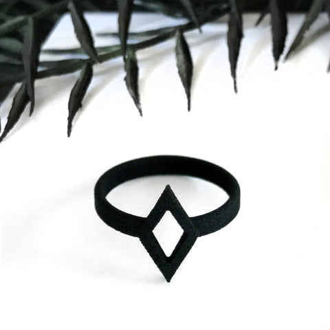 Bold graphic 3d printed black ring with diamond shaped outline design, displayed on white background with gothic black foliage border.