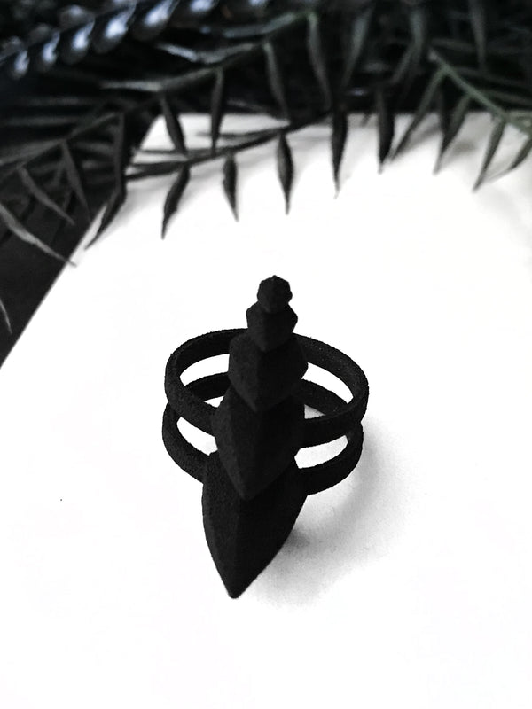 Front view, 3d printed black self defense ring with pyramid spikes, displayed on a white background with black foliage. Punk/gothic jewelry by Hypnovamp.