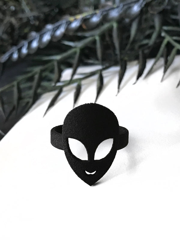 Black ring with classic 90s alien face. Displayed on a white background with black foliage. 3d printed jewelry by Hypnovamp.