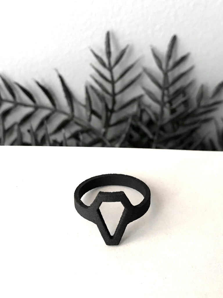 Simple black coffin ring against a white background with witchy black foliage. Minimalist 3d printed jewelry by Hypnovamp.
