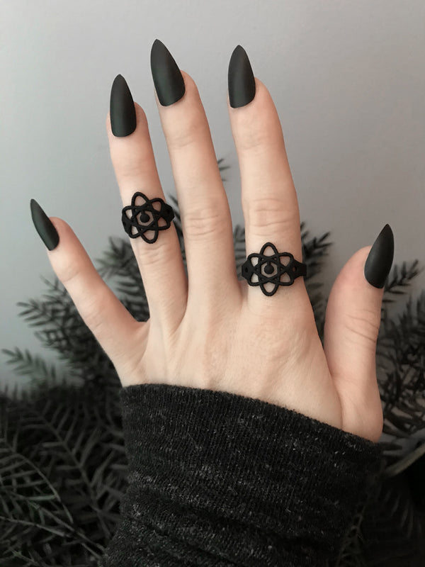 2 matte black atomic symbol rings on a witchy model's hand with long black fingernails. Gothic 3d printed science jewelry by Hypnovamp.