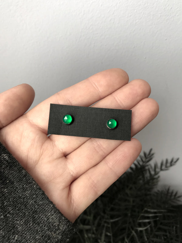 Witchy style stud earrings featuring oxidized sterling silver & rose-cut green onyx. Displayed in hand with black foliage in the background. Minimalist gothic jewelry handmade in Salem, MA by jewelry designer Hypnovamp.