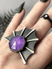 Close up view of handmade gothic bat ring with purple gemstone, worn on a witchy model hand with long black nails & a simple black ring. Handmade silver glow jewelry by Salem MA artistan Hypnovamp