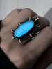 Night view of Blue glowing gemstone ring inspired by the Creature from the Black Lagoon, with sterling silver bat fins, displayed on a hand. Handmade gothic silver glow jewelry by Salem, MA artist Hypnovamp.
