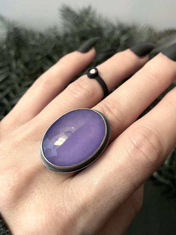 Lilac colored faceted rose quartz crystal ring displayed on a gothic model hand with long black nails and a black ring. Handmade silver glow in the dark jewelry by Salem, Massachusetts artist Hypnovamp.