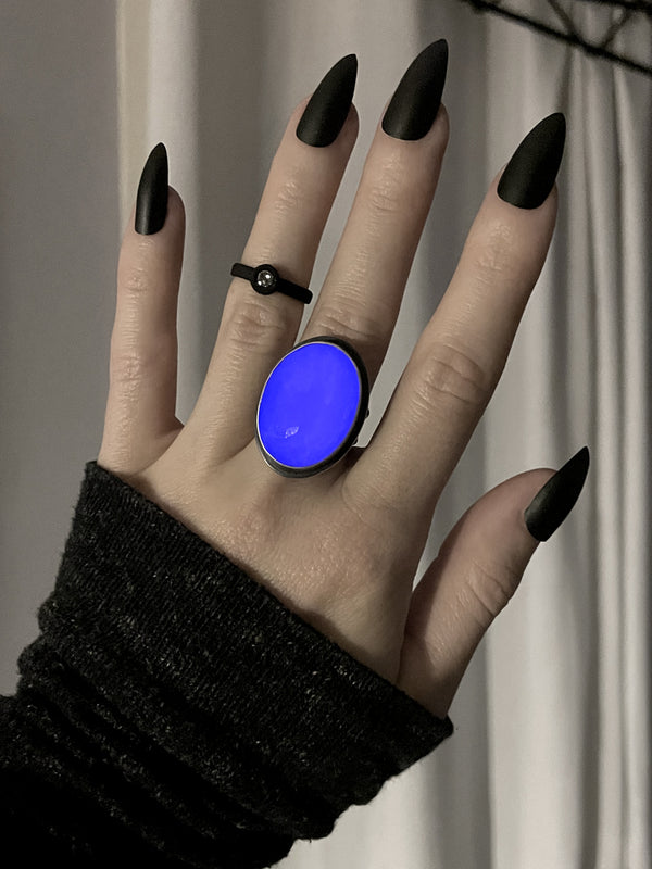 Glowing purple faceted rose quartz crystal ring displayed on a gothic model hand with long black nails and a black ring, in front of a white curtain. Handmade silver glow in the dark jewelry by Salem, Massachusetts artist Hypnovamp.