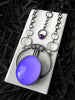 Handmade silver space-age art deco glowing purple necklace with faceted rose quartz and amethyst, displayed on a white tile against a floral black background. Fancy glow in the dark jewelry made by Salem, Massachusetts artist Hypnovamp.
