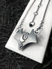 Backside detail of a handmade silver bat necklace with a crescent moon, star, and atomic diamond, displayed on a white tile against a black floral background. Witchy silver jewelry created by Salem, MA artist Hypnovamp.