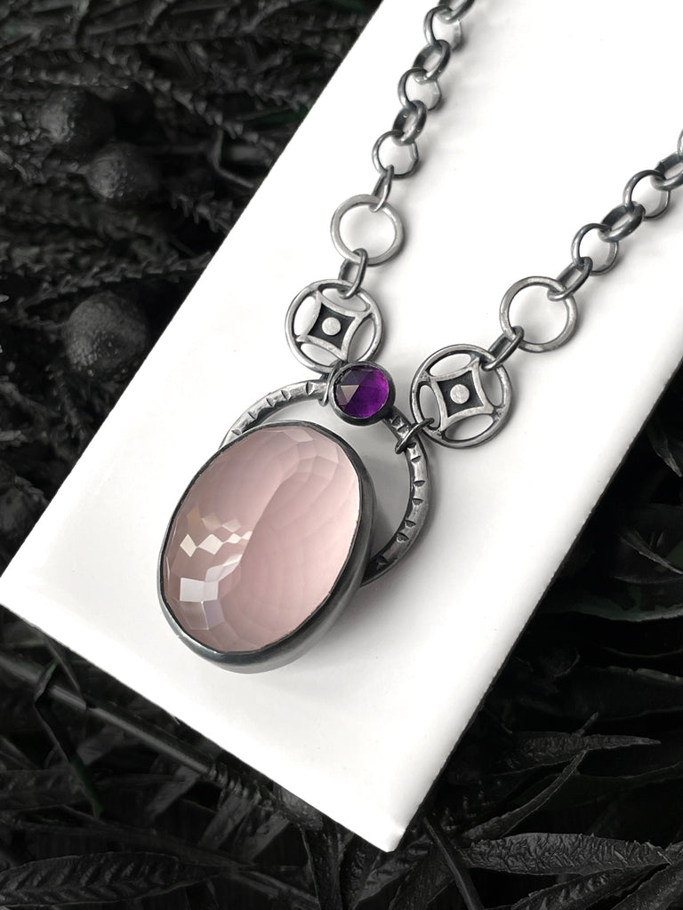 Handmade rose-quartz necklace with purple amethyst gemstone and fancy atomic diamond chain links, displayed on a white tile with a black floral background. Crystal glow in the dark jewelry made in Salem, Massachusetts by jewelry designer Hypnovamp.