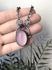 Handmade rose-quartz glow necklace with rose cut purple amethyst and atomic diamond chain links, held in a hand with black leaves in the background. Space age glow in the dark jewelry made by Salem, Massachusetts jewelry designer Hypnovamp.