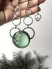Sparkly blue quartz crystal ball glow necklace with space age silver rings and white moonstone, held in a hand against a grey background with black foliage. Witchy glow in the dark jewelry handmade in Salem MA by jewelry designer Hypnovamp.