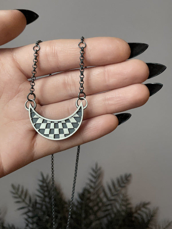 Warped checkerboard op art pattern inside a moon. Handmade silver necklace by Hypnovamp.