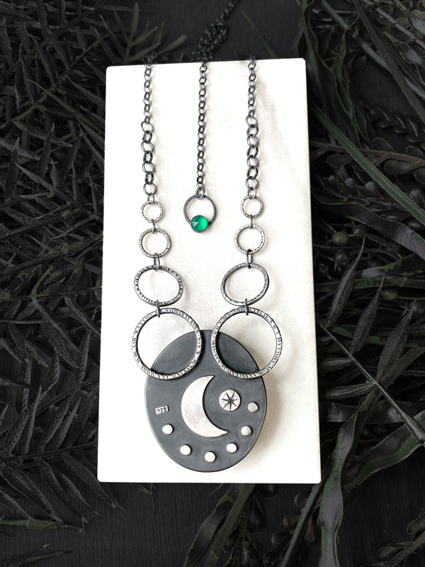 Back side details of handmade silver and quartz necklace featuring a crescent moon and star and rose cut green onyx gemstone. Displayed on a white tile with black foliage in the background. Horror and glow jewelry by Salem, MA artist Hypnovamp.