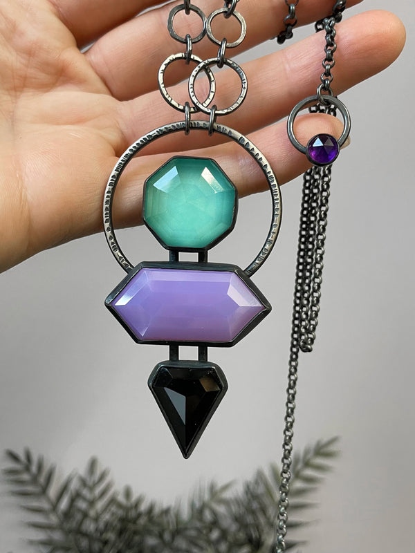 Space witchy statement glowing necklace with art deco style & 80s mall colors, displayed in a hand. High quality handmade glow in the dark jewelry by Hypnovamp.