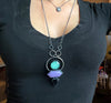 Space witchy statement glowing necklace with art deco style & 80s mall colors, being work by a woman in a black shirt. High quality handmade glow in the dark jewelry by Hypnovamp.