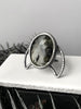 Witchy black rutilated quartz ring with a crescent moon shape, displayed on white tile with gothic black foliage. Sterling silver glow jewelry handmade in Salem, MA by artist Hypnovamp.