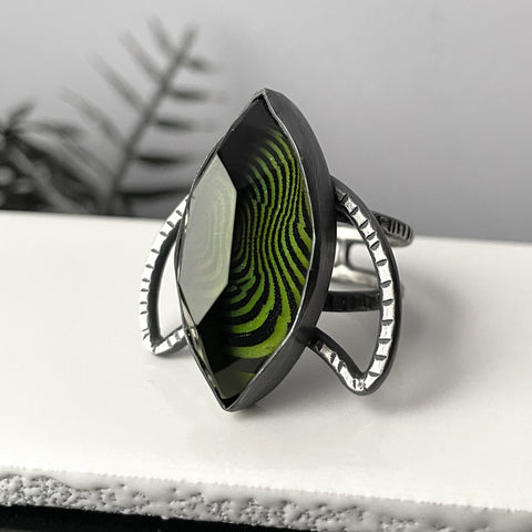 Handmade silver glow ring with trippy op art pattern under a marquise shaped stone, set on a silver crescent moon. High quality glow in the dark jewelry made in Salem, MA by artist Hypnovamp.