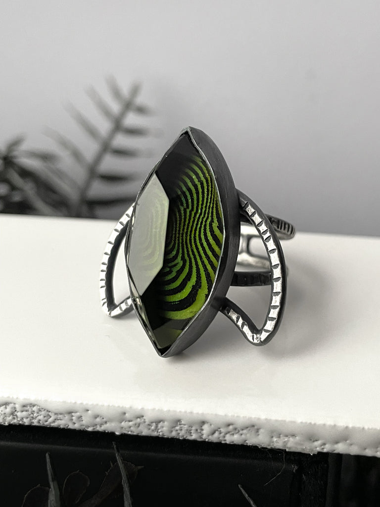 Handmade silver glow ring with trippy op art pattern under a marquise shaped stone, set on a silver crescent moon. High quality glow in the dark jewelry made in Salem, MA by artist Hypnovamp.