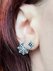 Handmade sterling silver stud earrings with a mid century modern atomic diamond design, displayed along with silver spiderweb earrings in the ear of a red headed model. Witchy retro jewelry handmade in Salem, MA by artist Hypnovamp.