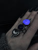 Night view of space queen statement ring with blue lapis lazuli, glowing purple rutilated quartz, & clear quartz with a silver moon, displayed on a witchy model's hand with long black nails. High quality handmade silver glow in the dark jewelry by Hypnovamp.